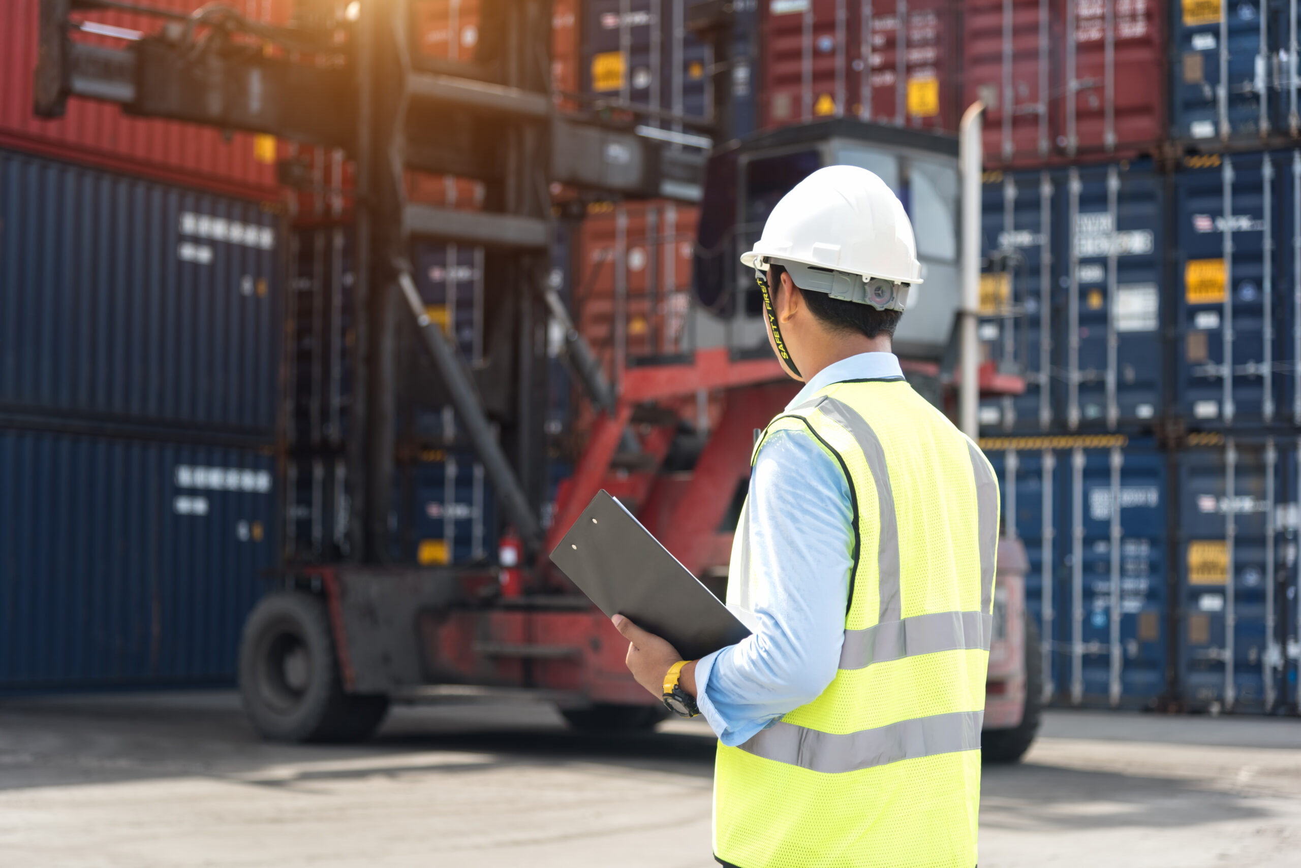 A worker in a high-visibility vest and hard hat standing in a loading freight area, representing workplace health and safety compliance.