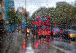 London bus seen through bus stop glass during autumn rain, representing urban traffic and bus incidents.