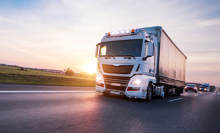 White articulated lorry driving along a motorway with cars behind it at sunset.