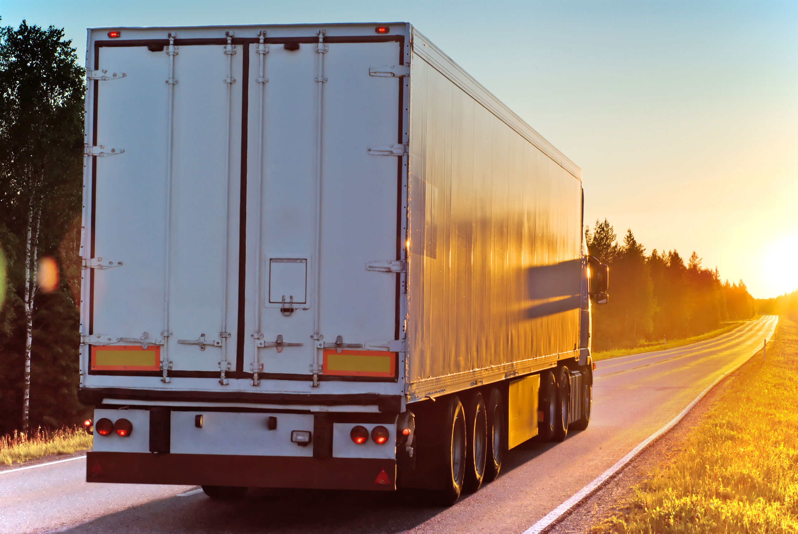 White haulage truck driving on a road at sunset.
